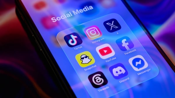 A folder of social media applications, including TikTok, Instagram, X (formerly Twitter), Snapchat, YouTube, Facebook, Threads, Discord, and Messenger, is displayed on a smartphone screen placed on a reflective surface onto which a colorful abstract illus